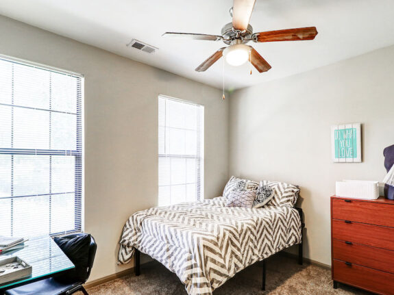 Two window student bedroom with drawer, ceiling fan and desk on the corner.