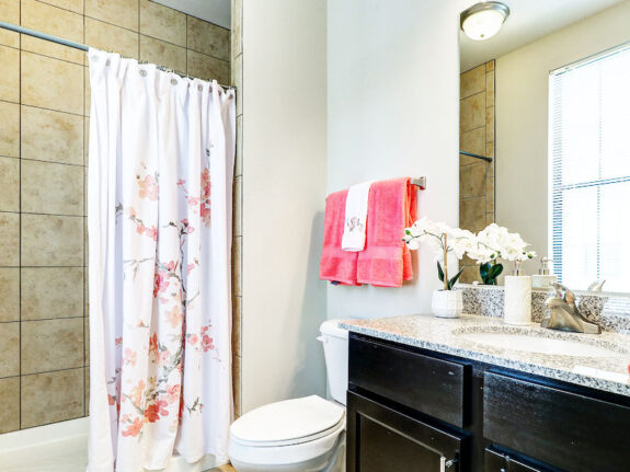 Townhome bathroom with pink towels, black drawers and flower patter on shower curtain.